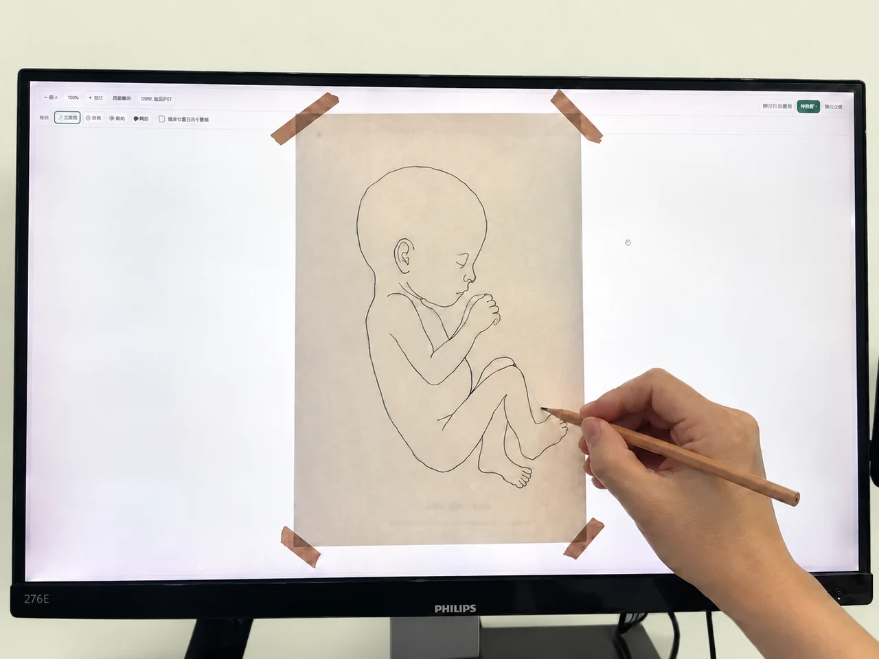 A hand lightly tracing the baby's outline onto paper held against a computer screen